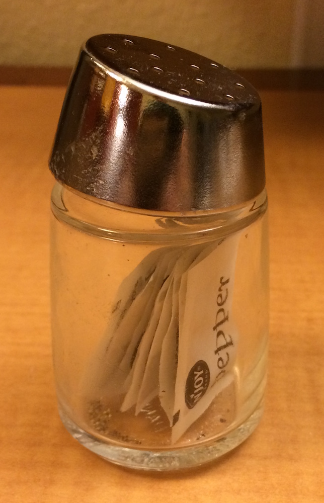 A pepper shaker containing several individual paper packets of pepper